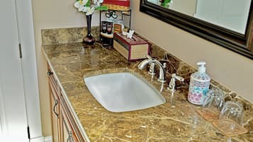 Un baño con lavamanos de mármol, espejo, dispensador de jabón y un pequeño estante con artículos de aseo.