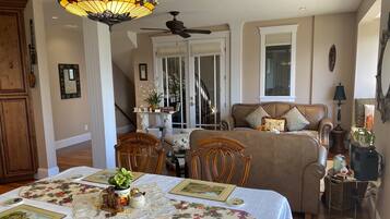 A cozy living room with a dining table set for four, a sofa, and a ceiling fan.