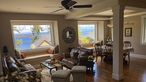 A spacious living room with a view of the water, a ceiling fan, and a dining area with a table and chairs.