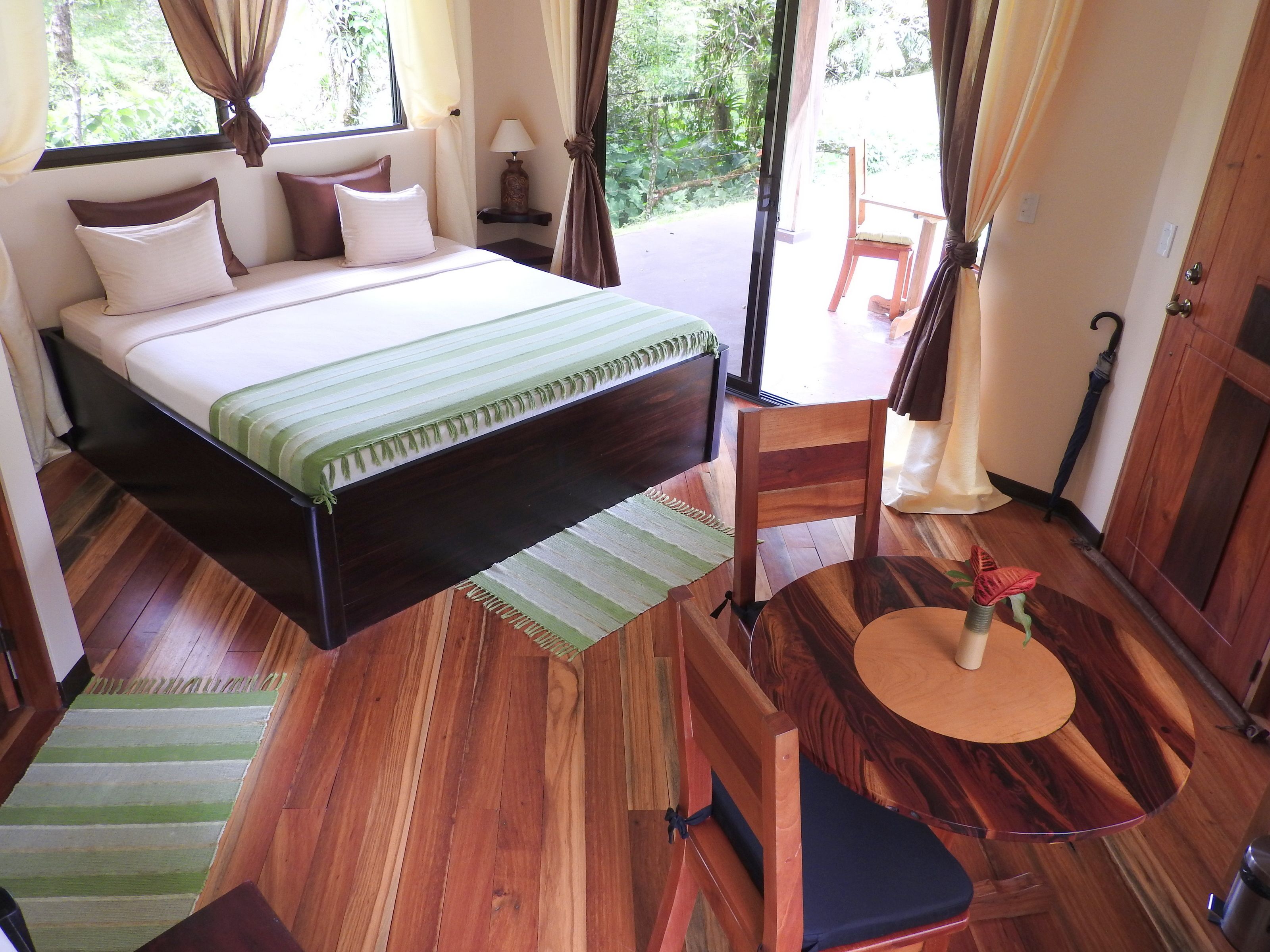 A bedroom with a bed, a wooden chair, a small table, and a view of the outdoors.
