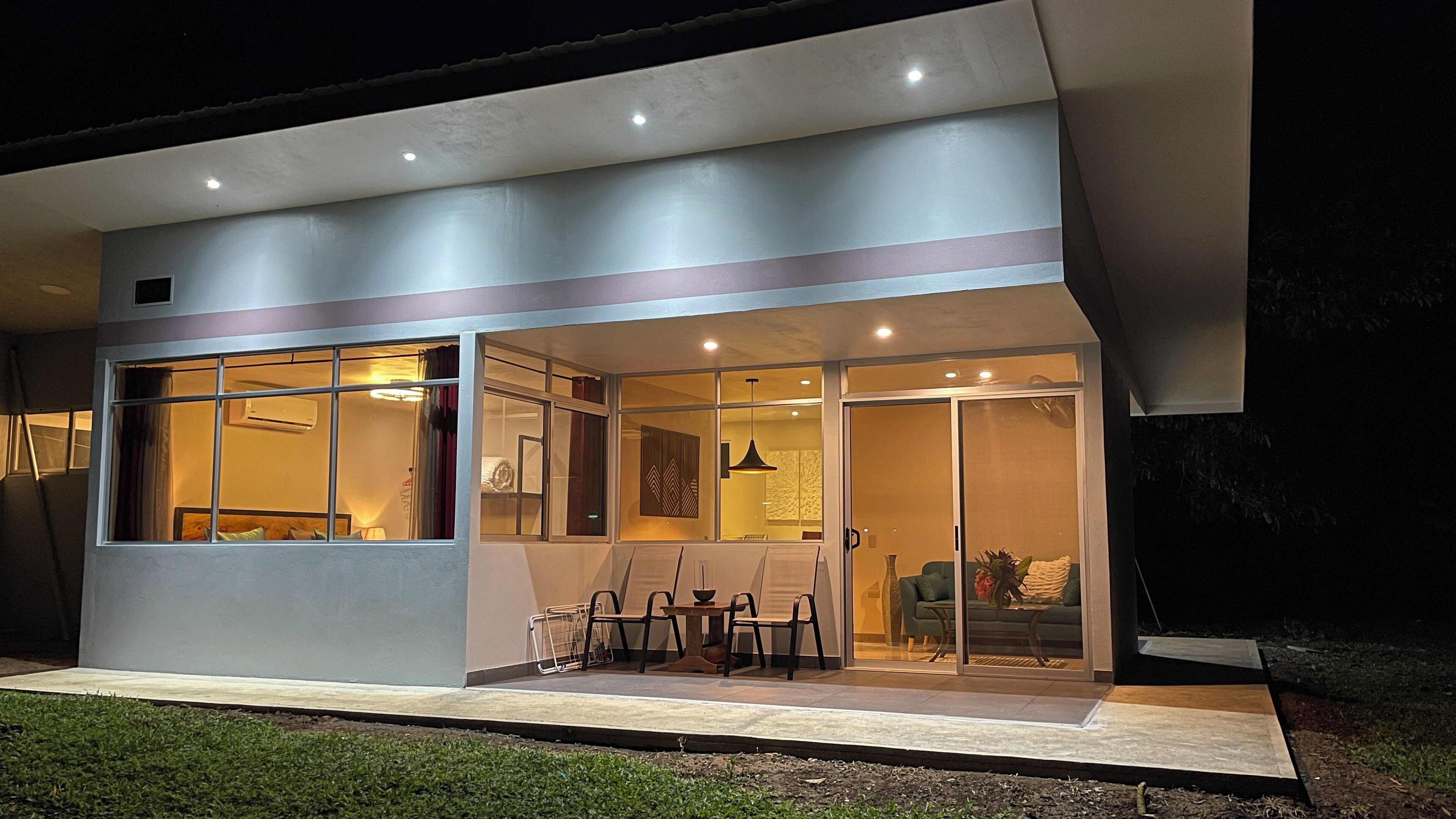 Un edificio moderno con ventanas amplias, un patio con sillas y una mesa de comedor.