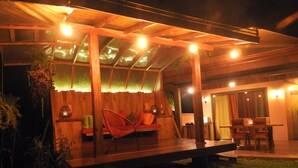 A wooden outdoor seating area with a bench and chairs, a table, and a lantern.