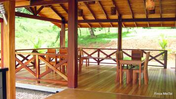 Una terraza de madera al aire libre con un área de estar cubierta, barandas de madera y vistas a un paisaje verde.