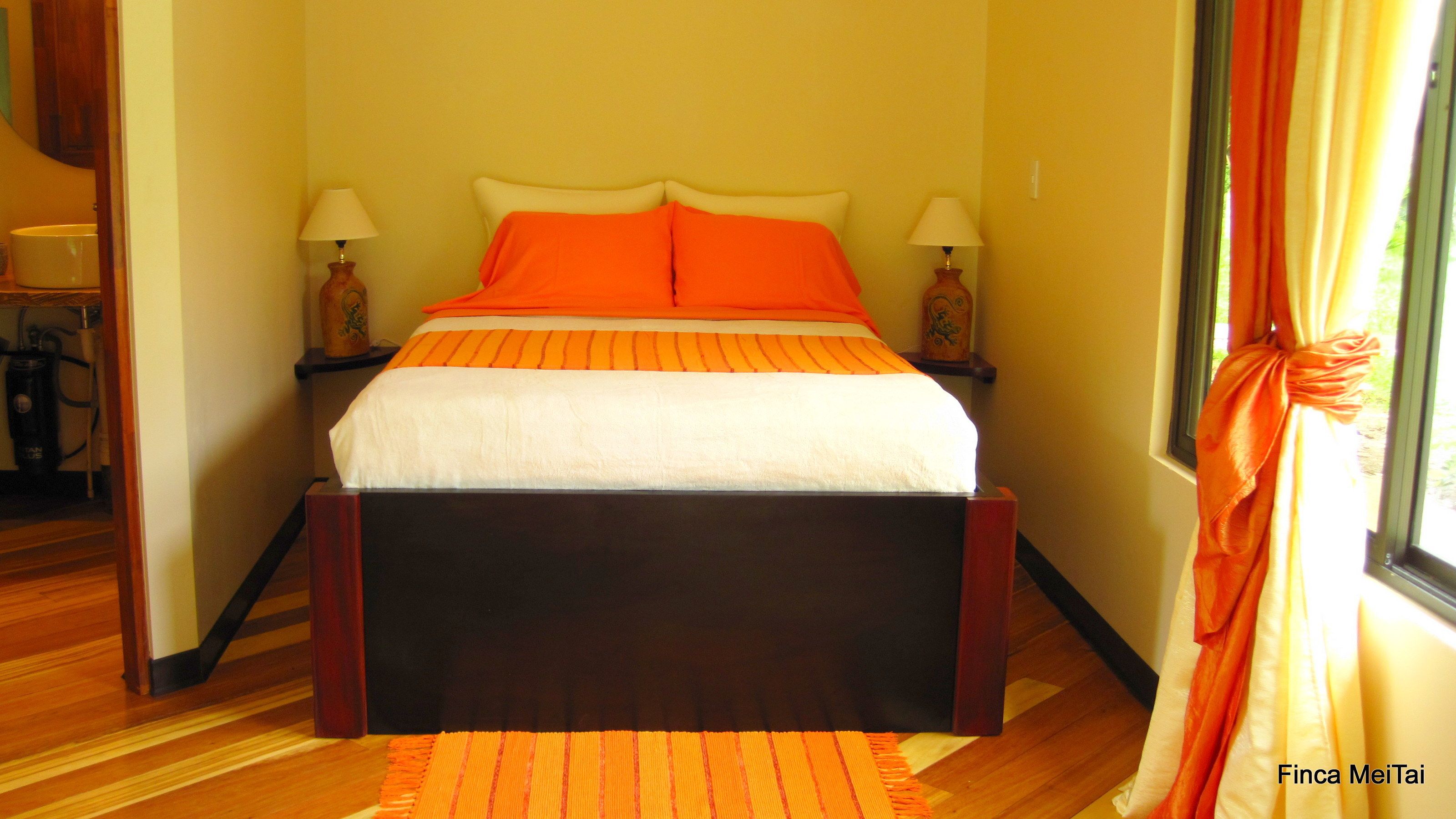 Uma cama com roupa de cama laranja, duas luminárias de cabeceira e uma cabeceira de madeira.
