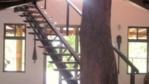 A large wooden tree trunk supporting a staircase in a spacious room with large windows.