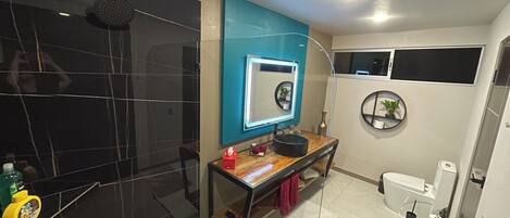 Un baño moderno con un espejo grande, baldosas negras, un tocador de madera y un inodoro.