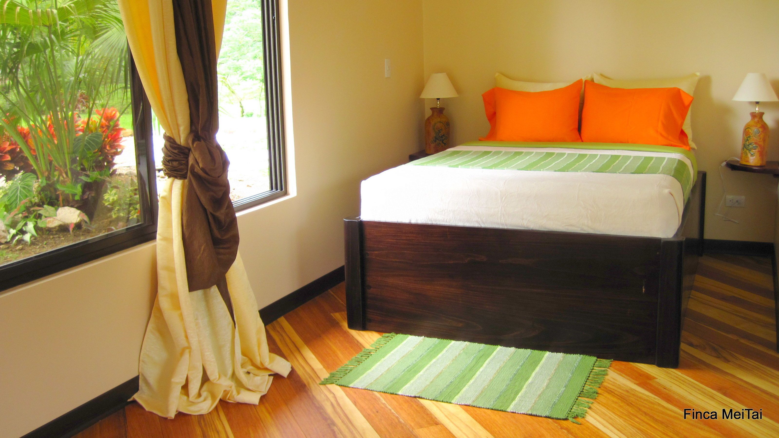 Un dormitorio con cama, cortinas, una ventana, una mesita de noche y una lámpara.