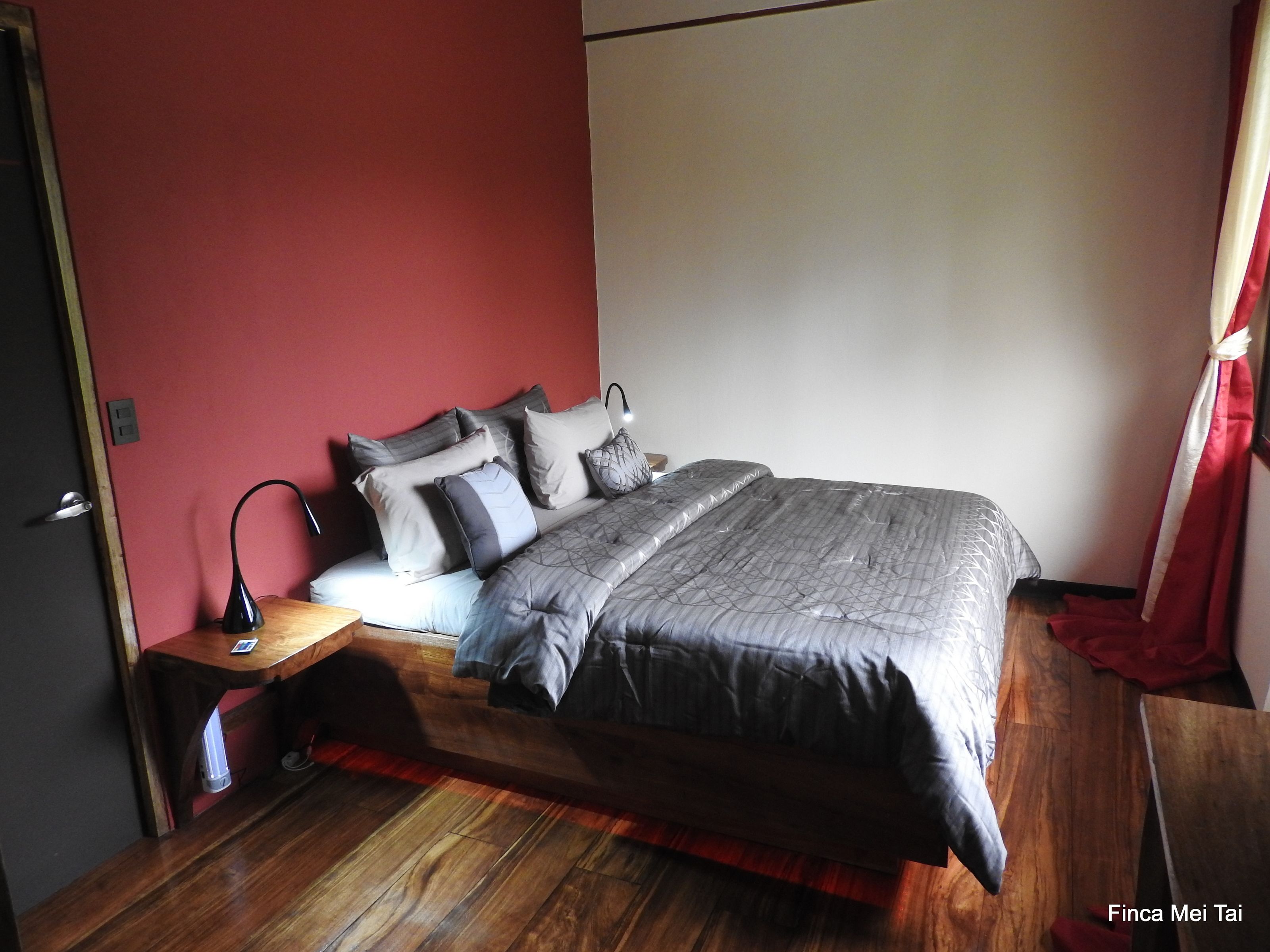 Un dormitorio con cama, mesita de noche, lámpara y una cortina roja.