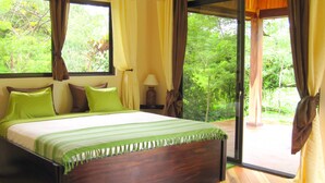 A bedroom with a large bed, a nightstand, a lamp, and a window with curtains.