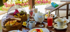 A breakfast setting with a basket of fruits, croissants, and a glass of juice on a table.