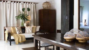 Una sala de estar con sofá, un aparador de madera, una mesa de comedor y un amplio ventanal con cortinas.