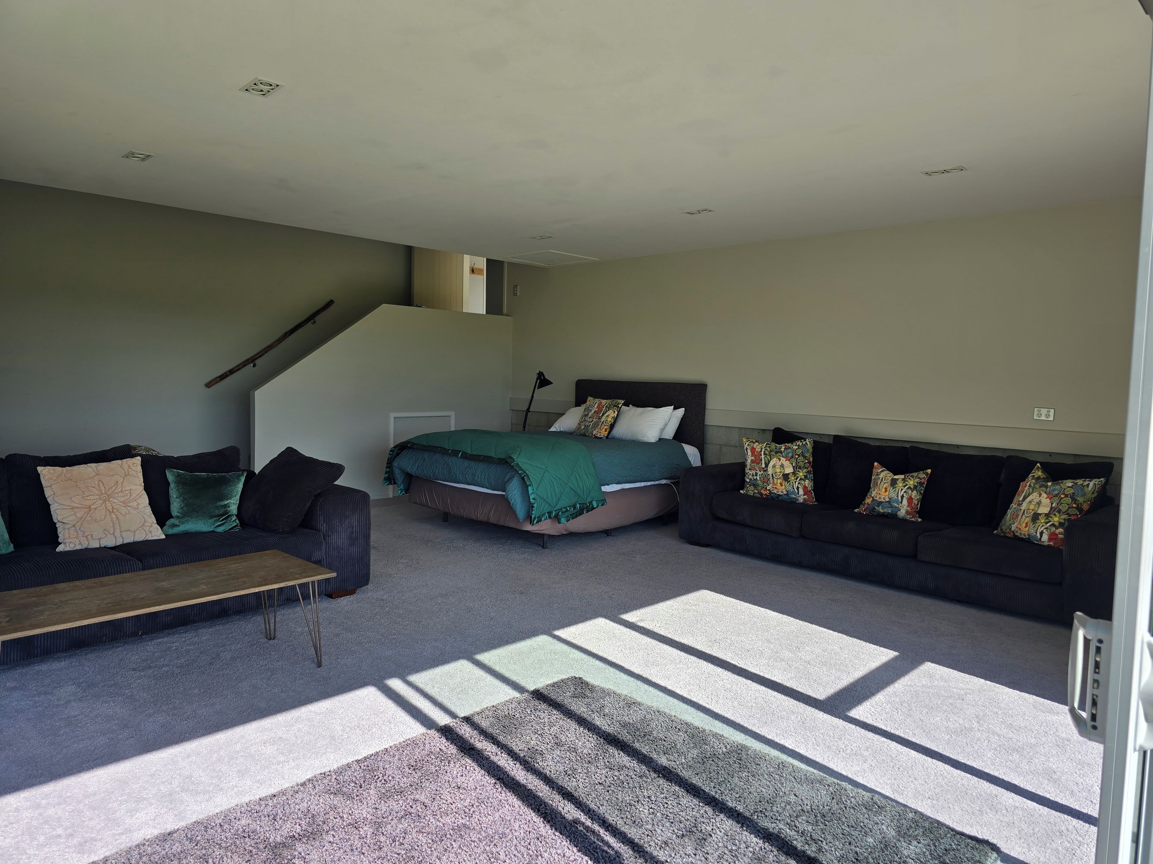 A spacious living room with a bed, two sofas, and a staircase.