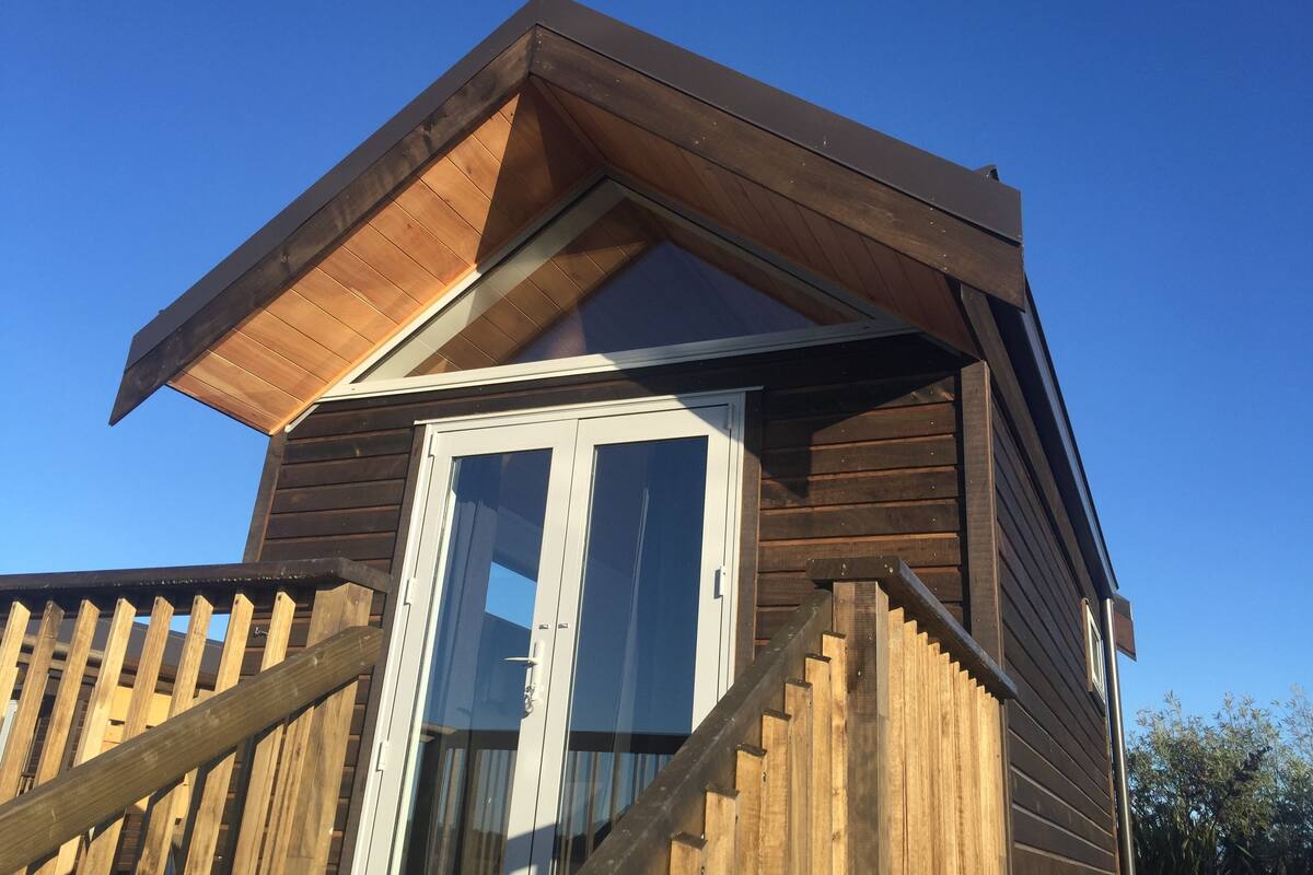 A wooden cabin with a sloped roof, a glass door, and a wooden staircase leading to the entrance.