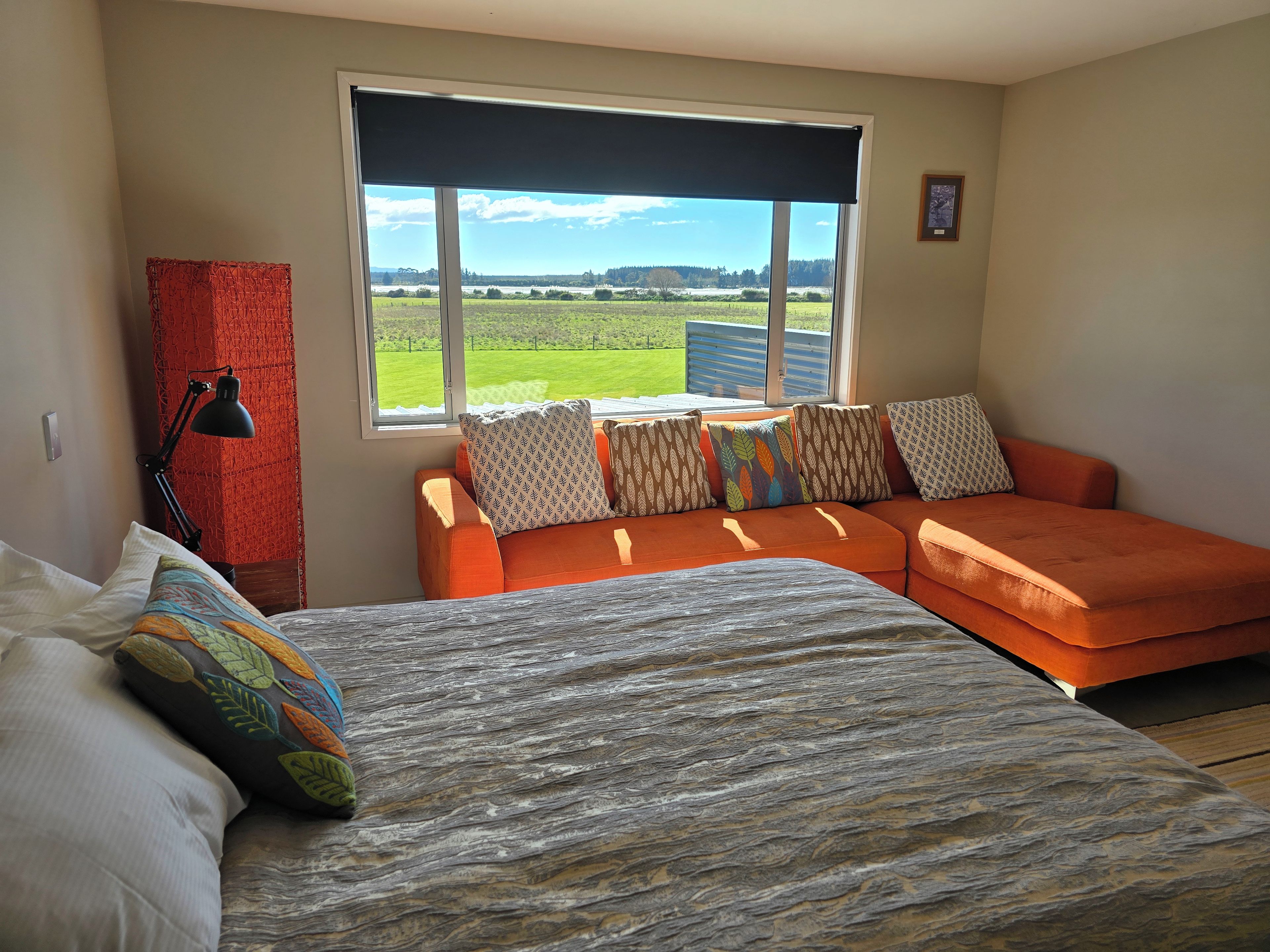 A room with a bed, a sofa, a desk with a lamp, and a window with a view of a field.