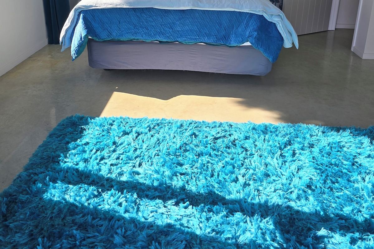 A bedroom with a bed, a blue rug, a patterned wallpaper, and a door.