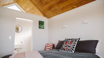 A bedroom with a wooden ceiling, a bed with a grey and black duvet, a red and white striped pillow, and a black pillow with a white design.