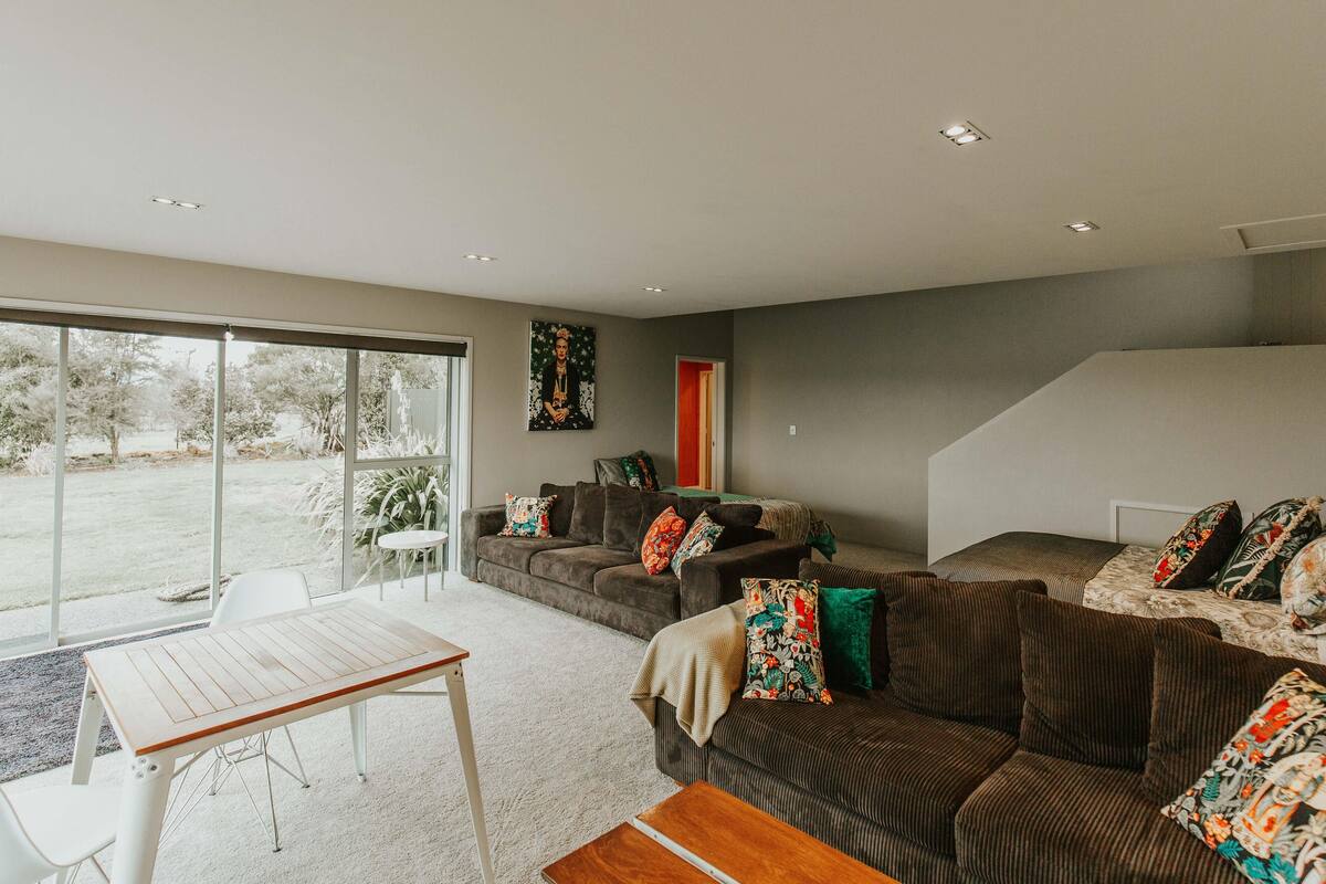 A modern living room with a large window, a sofa set, a dining table, and a staircase.