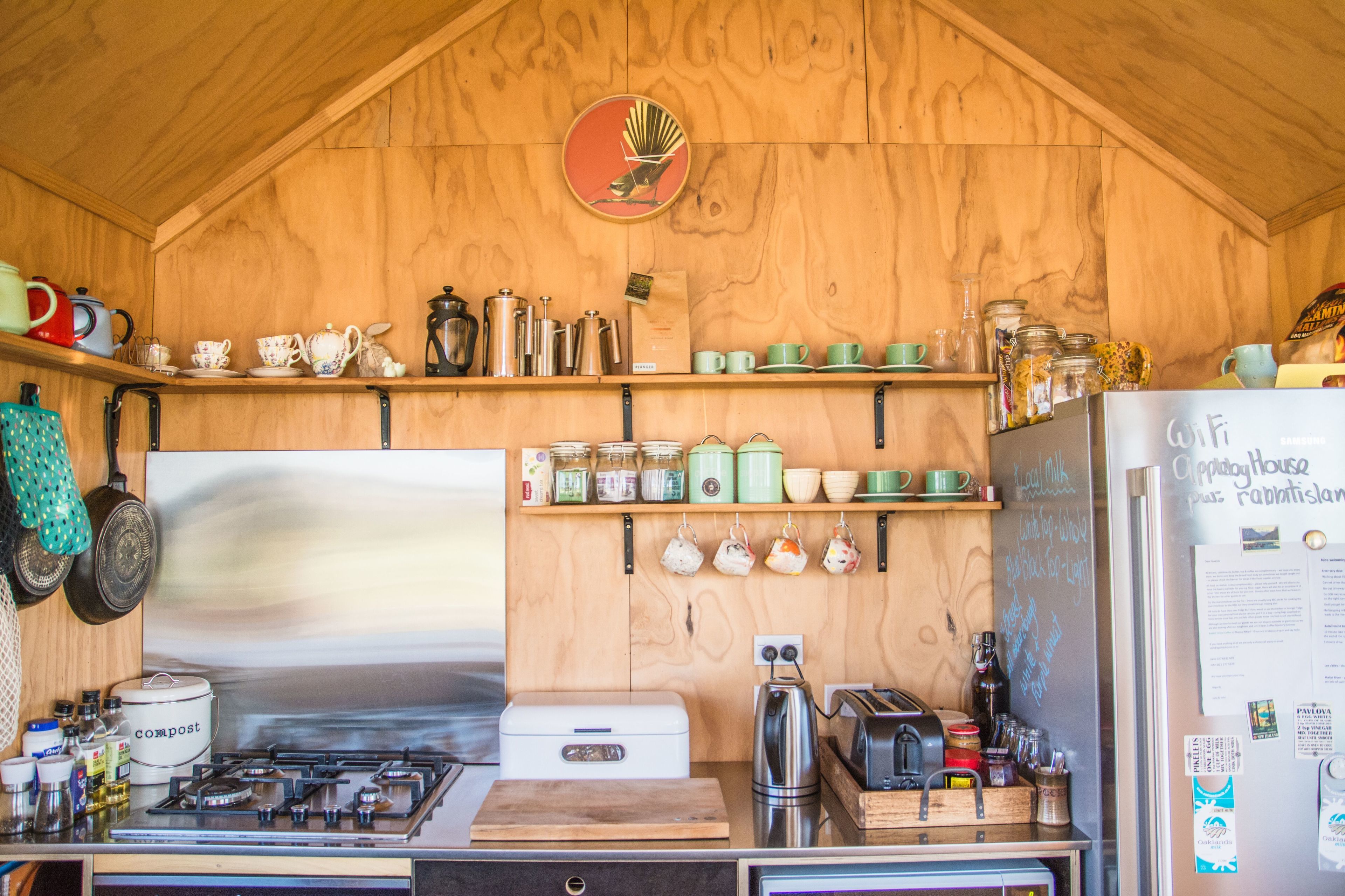 A rustic kitchen with wooden walls, a stainless steel stove, and various kitchen utensils and appliances.
