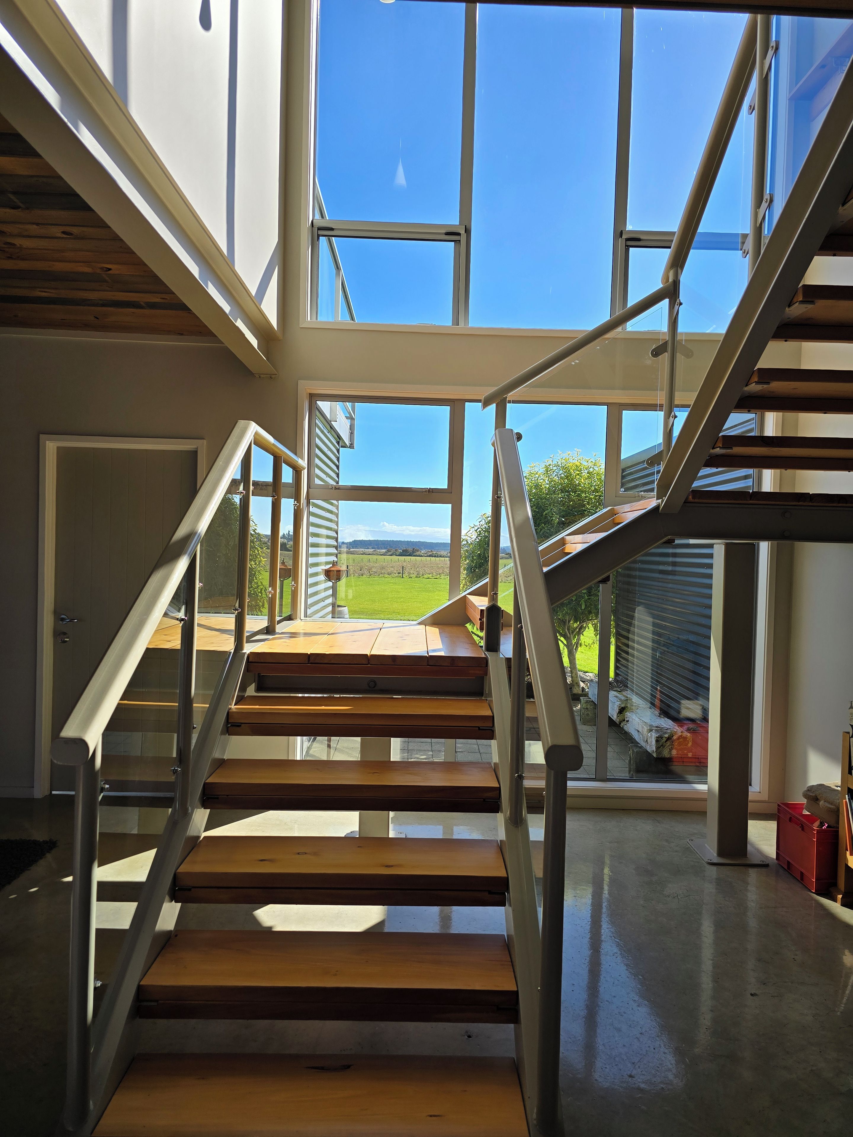 Ein modernes Interieur mit einer Treppe zu einem Außenbereich, großen Fenstern und Blick ins Grüne.