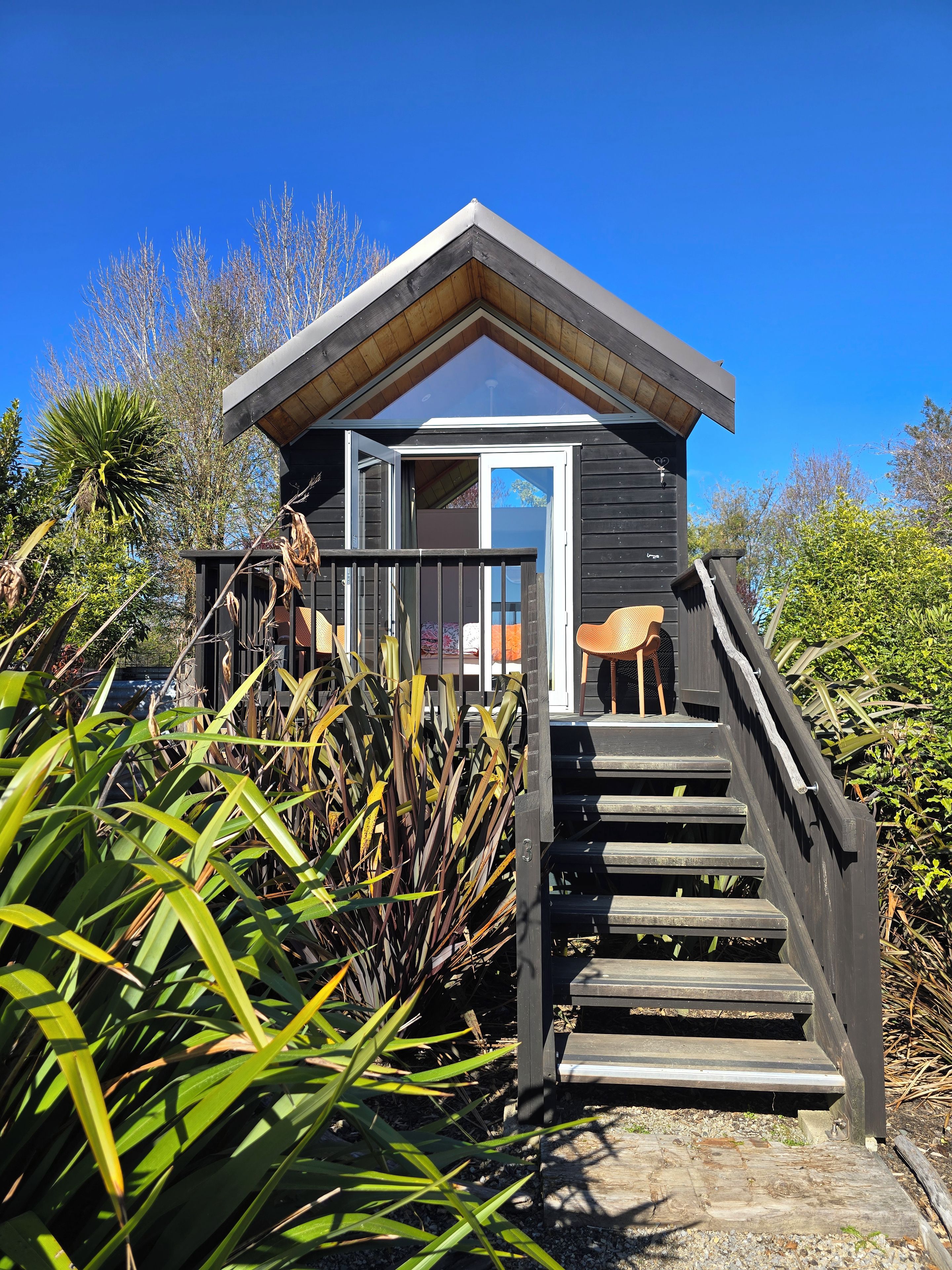A wooden cabin with a balcony, a staircase leading up to it, and surrounding vegetation.
