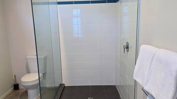 A modern bathroom with a glass-enclosed shower, a toilet, and a towel rack.