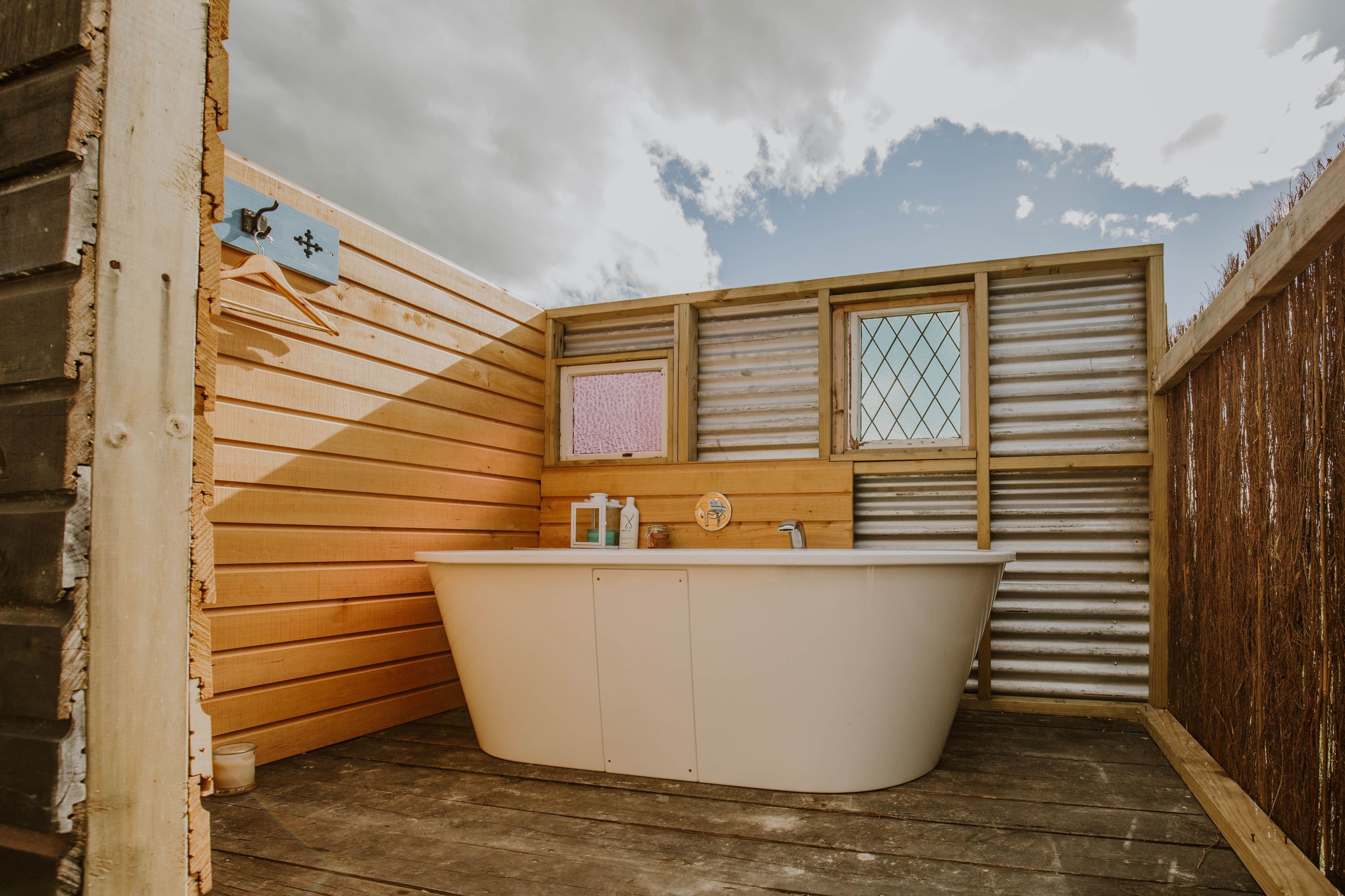 A wooden cabin with a wooden interior, a white bathtub, and a window with a metal grid.