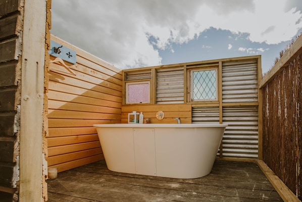 A wooden cabin with a wooden interior, a white bathtub, and a window with a metal grid.