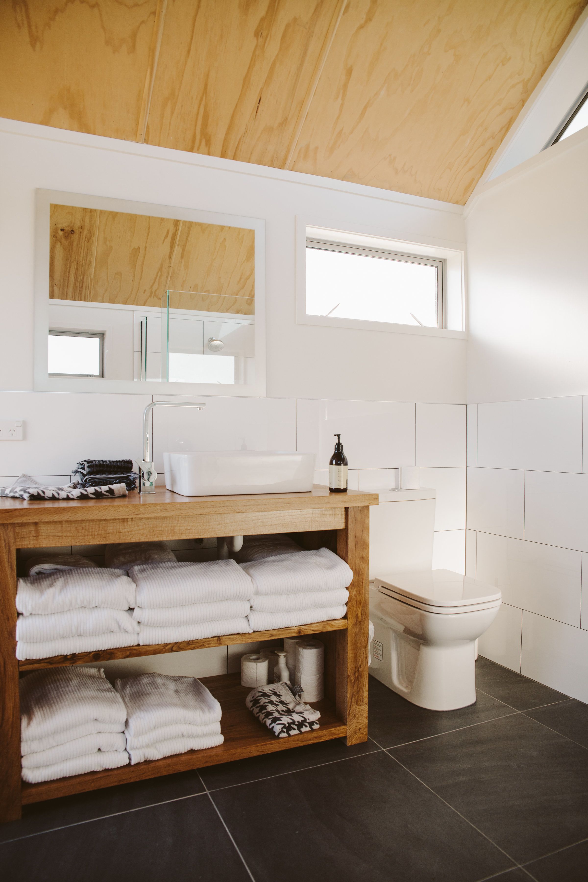 A modern bathroom with a wooden vanity, white sink, and a toilet.