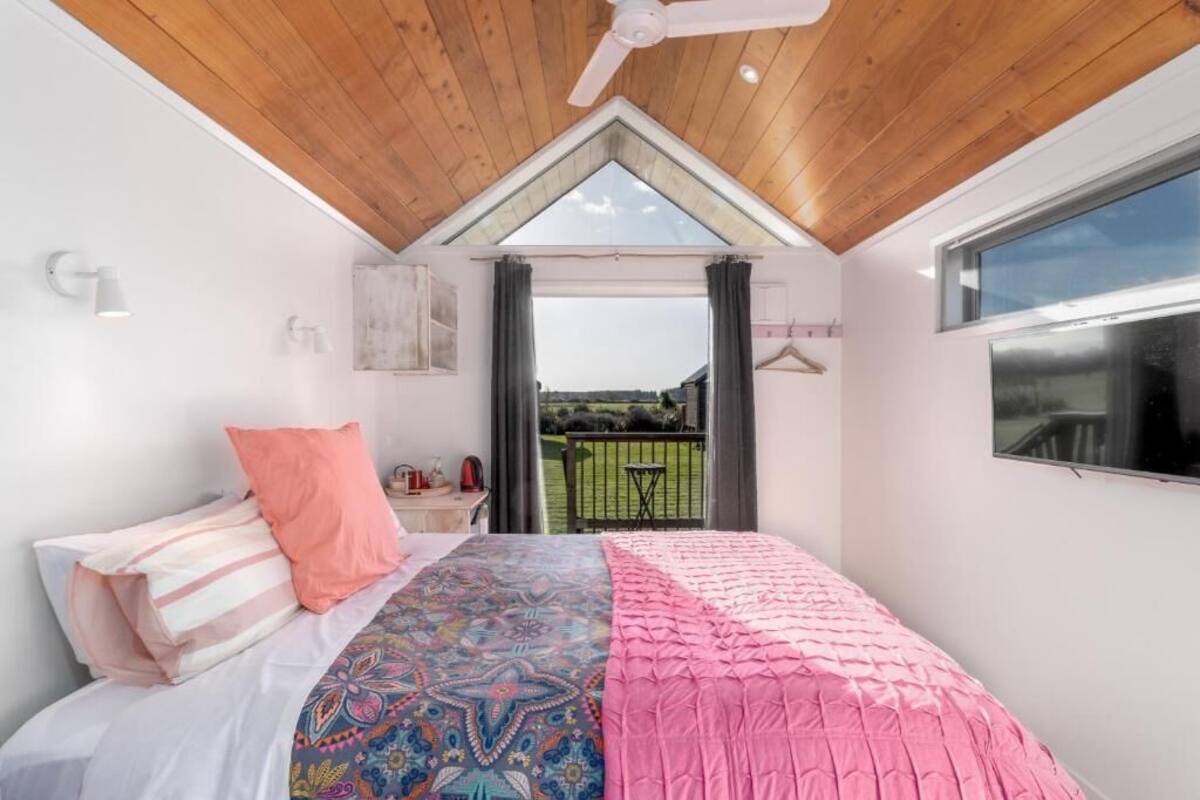 A bedroom with a large bed, a ceiling fan, a window, and a balcony with a view of the countryside.