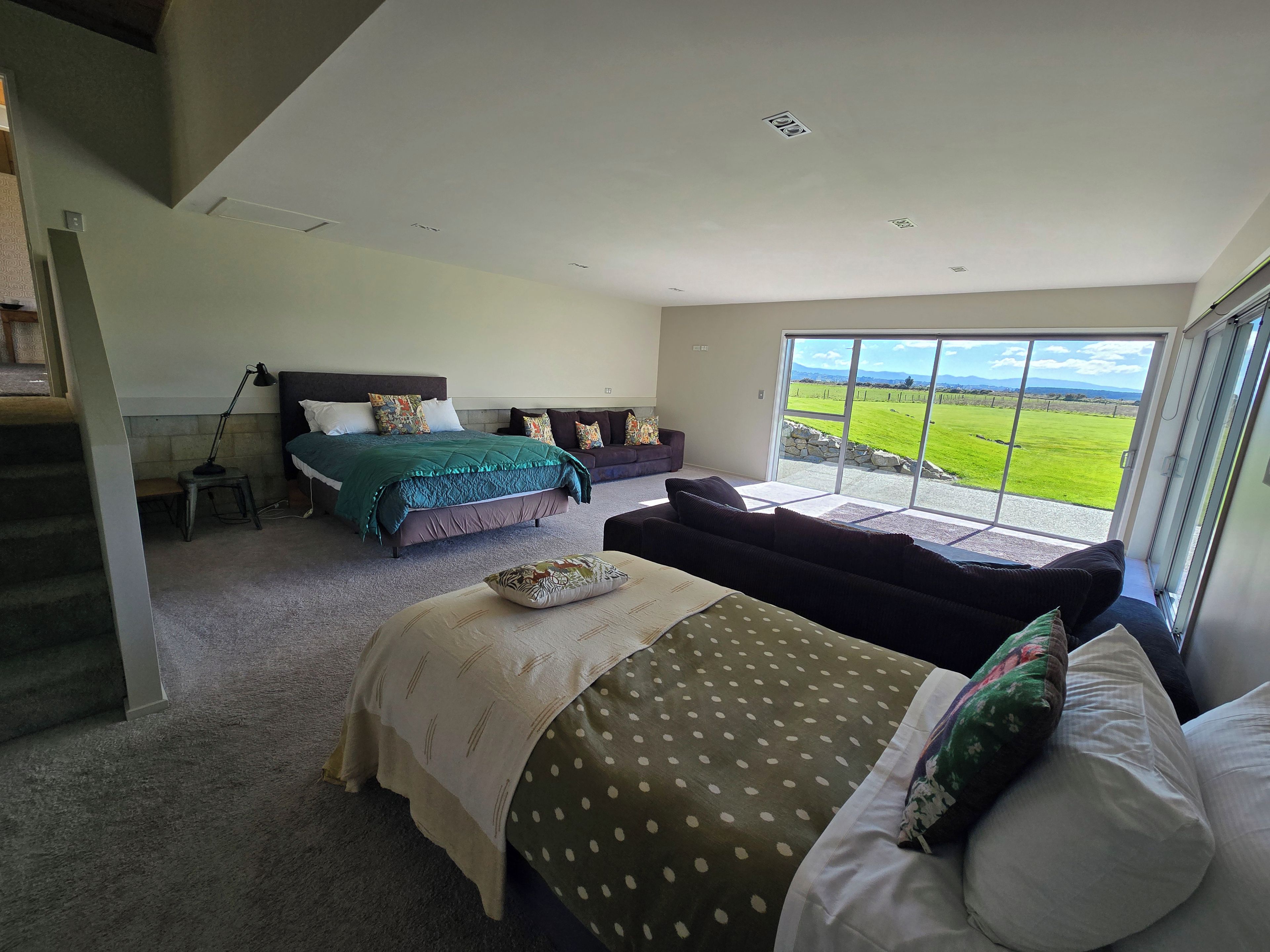 Ein geräumiges Schlafzimmer mit einem großen Bett, einer Couch und Blick auf ein grünes Feld durch eine Glastür.