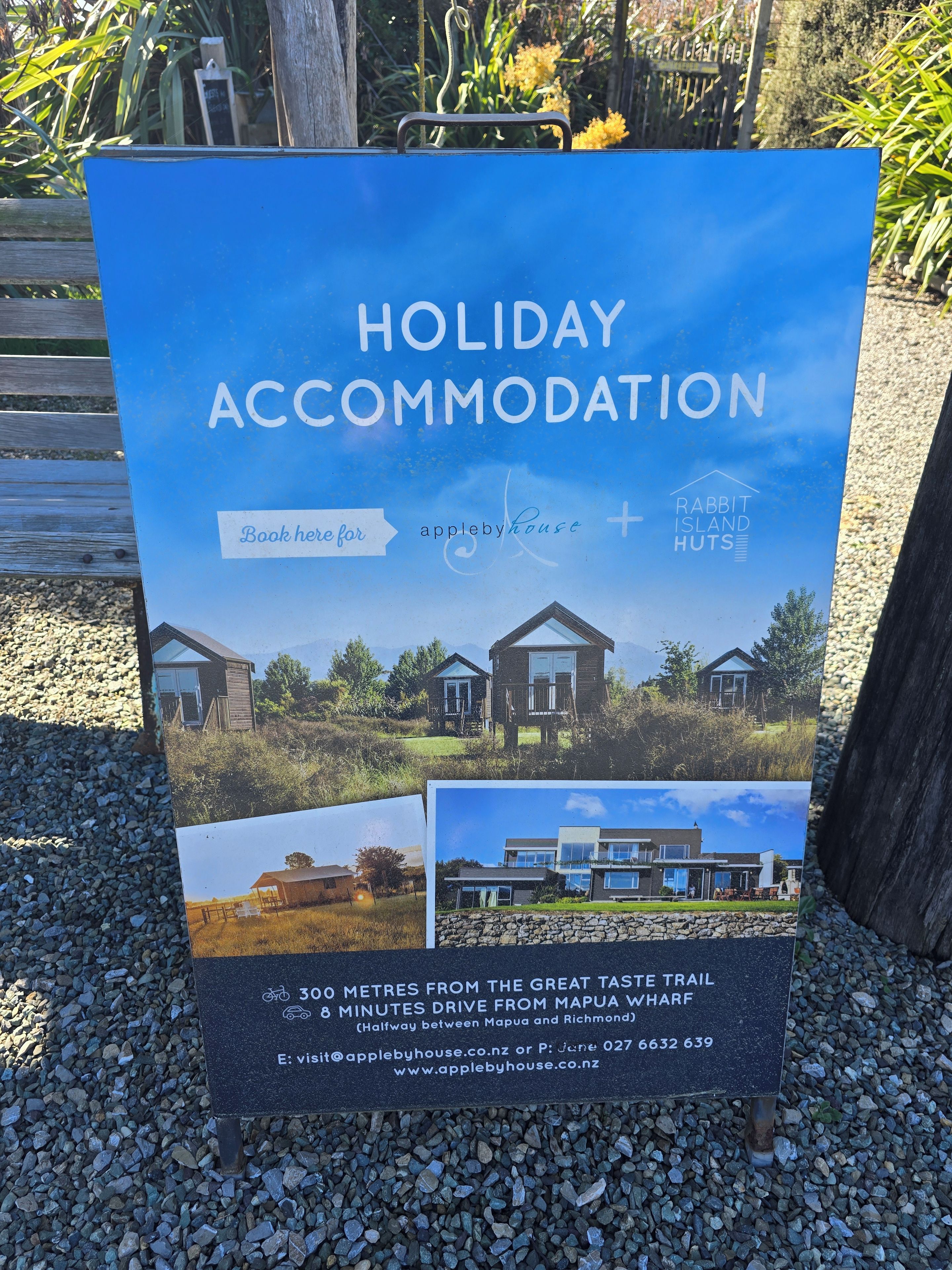 A sign for holiday accommodation advertising a property with a view of a house, a mountain, and a lake.