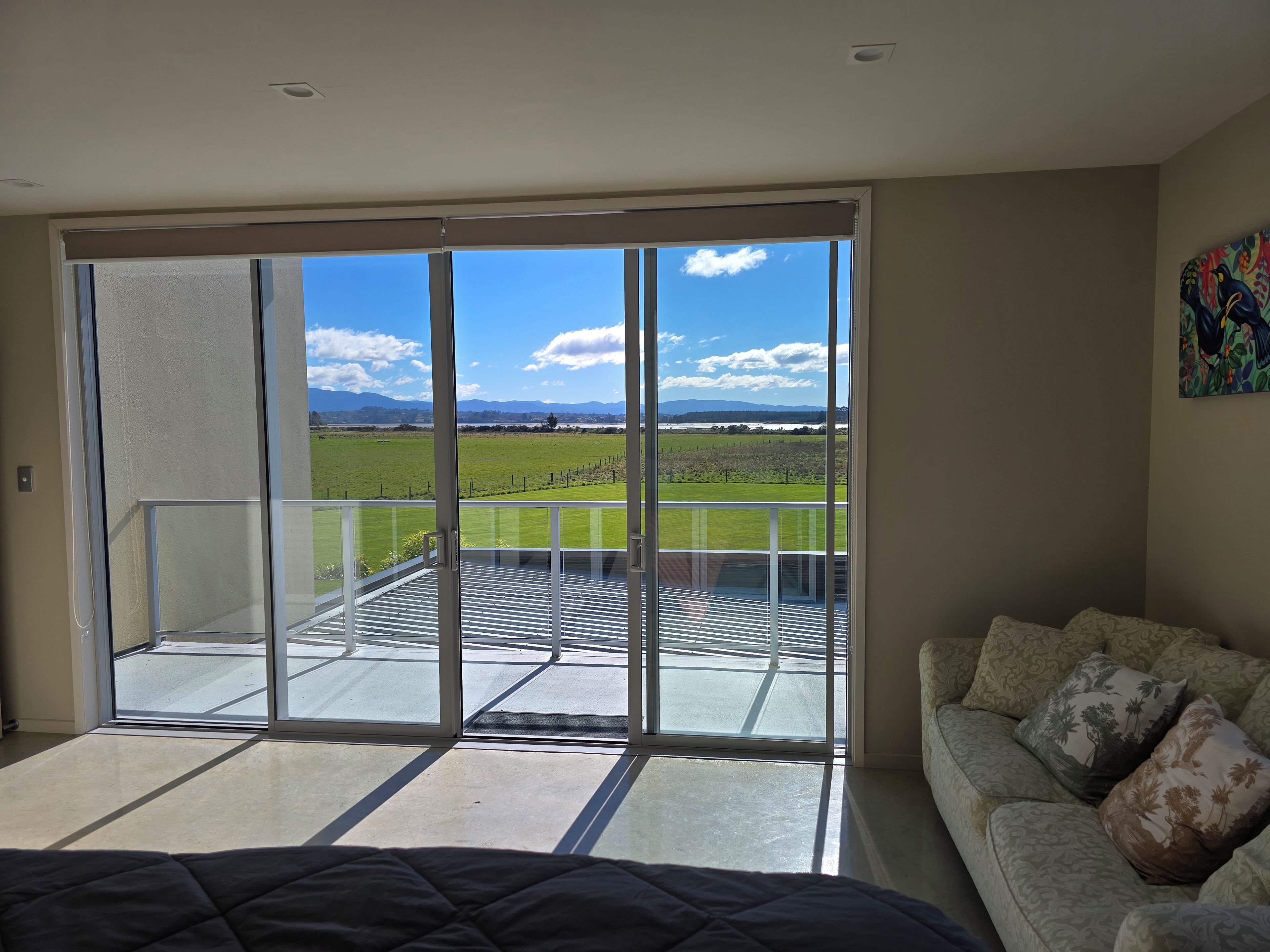 A room with a large sliding glass door leading to a balcony with a view of a green field and mountains.