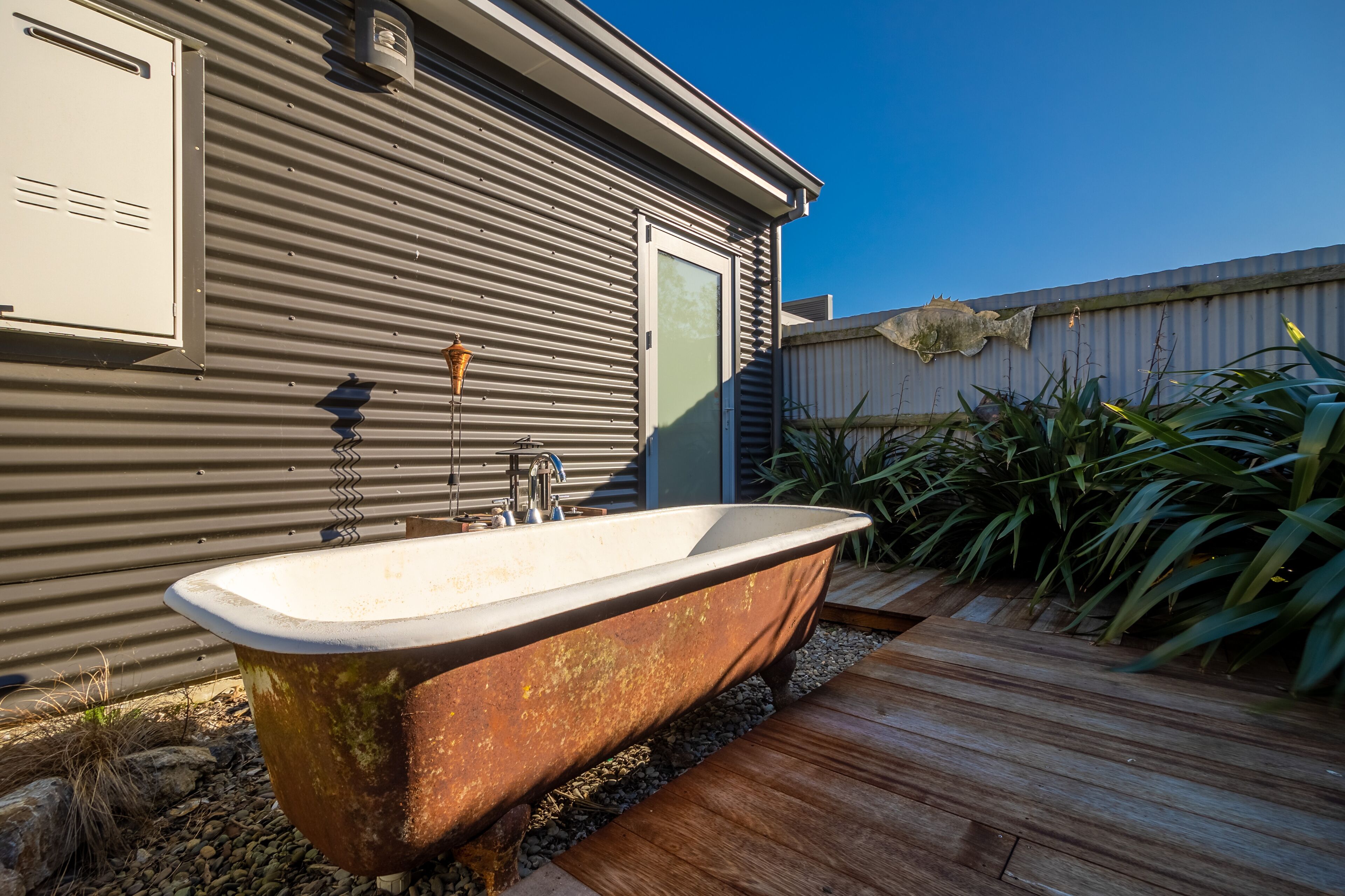 Une baignoire extérieure rustique, installée à côté d’un bâtiment en métal doté d’une terrasse en bois.