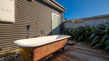 Une baignoire extérieure rustique, installée à côté d’un bâtiment en métal doté d’une terrasse en bois.
