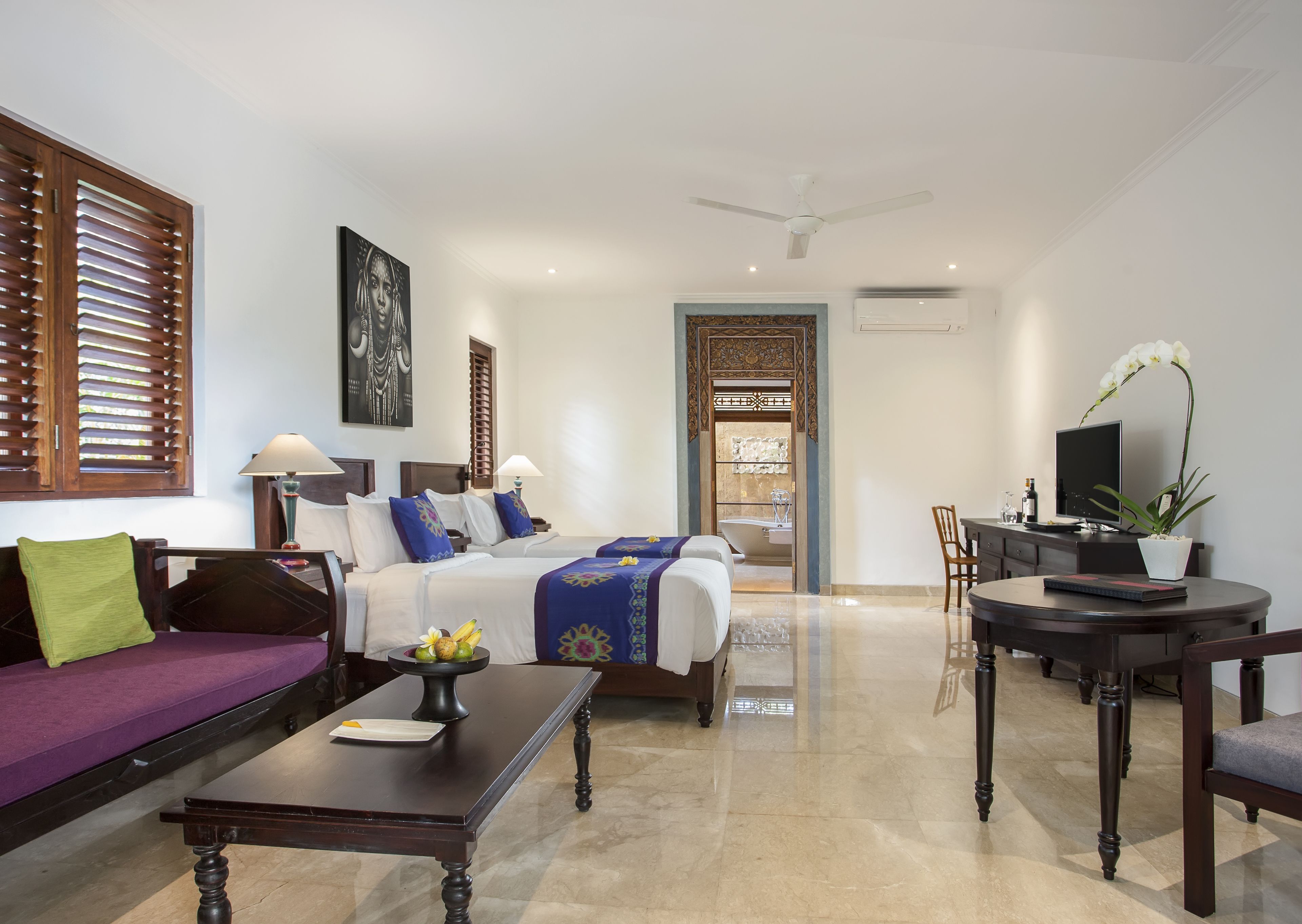 A hotel room with a bed, a sofa, a dining table, a TV, and a bathroom visible through an open door.