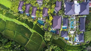 Una vista aerea di un resort con diverse ville, una zona piscina centrale e vegetazione lussureggiante circostante.