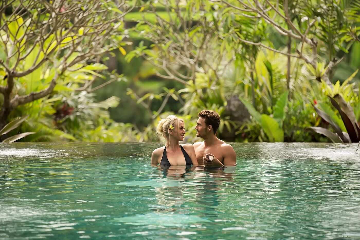 Una pareja en una piscina cristalina rodeada de abundante vegetación.