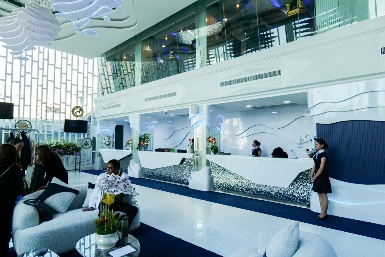 En modern hotellobby med en receptionsdisk, en sittgrupp och en trappa som leder upp till en övre våning.