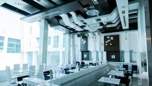 A modern restaurant with a long counter, white chairs, and a chandelier. - Glacier Hotel Khon Kaen (Khon Kaen)