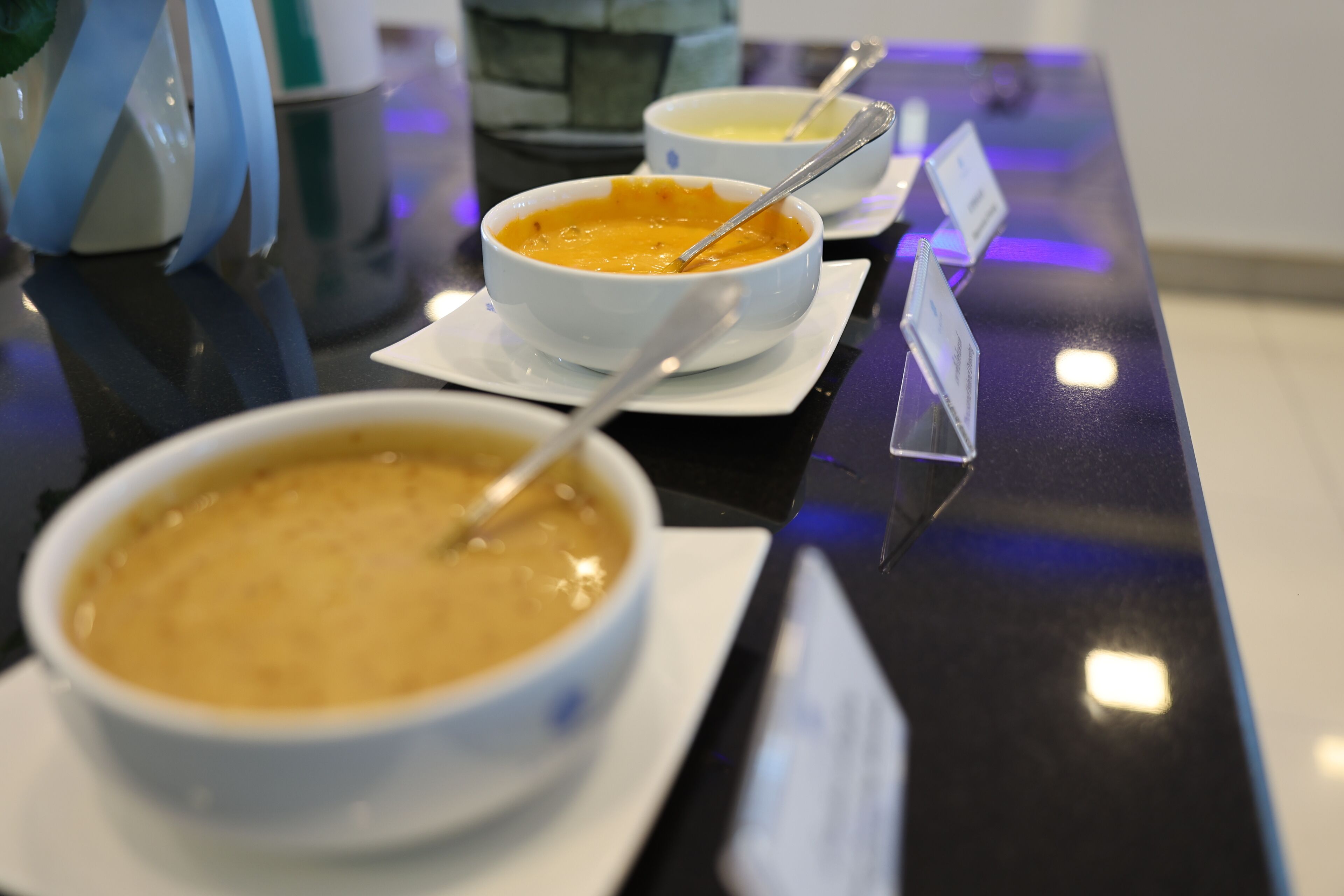 Tres tazones de sopa sobre una mesa negra reflectante con tarjetas de nombres.