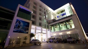 A multi-story hotel with a modern design, featuring a large entrance and a parking area with several vehicles. - Glacier Hotel Khon Kaen (Khon Kaen)