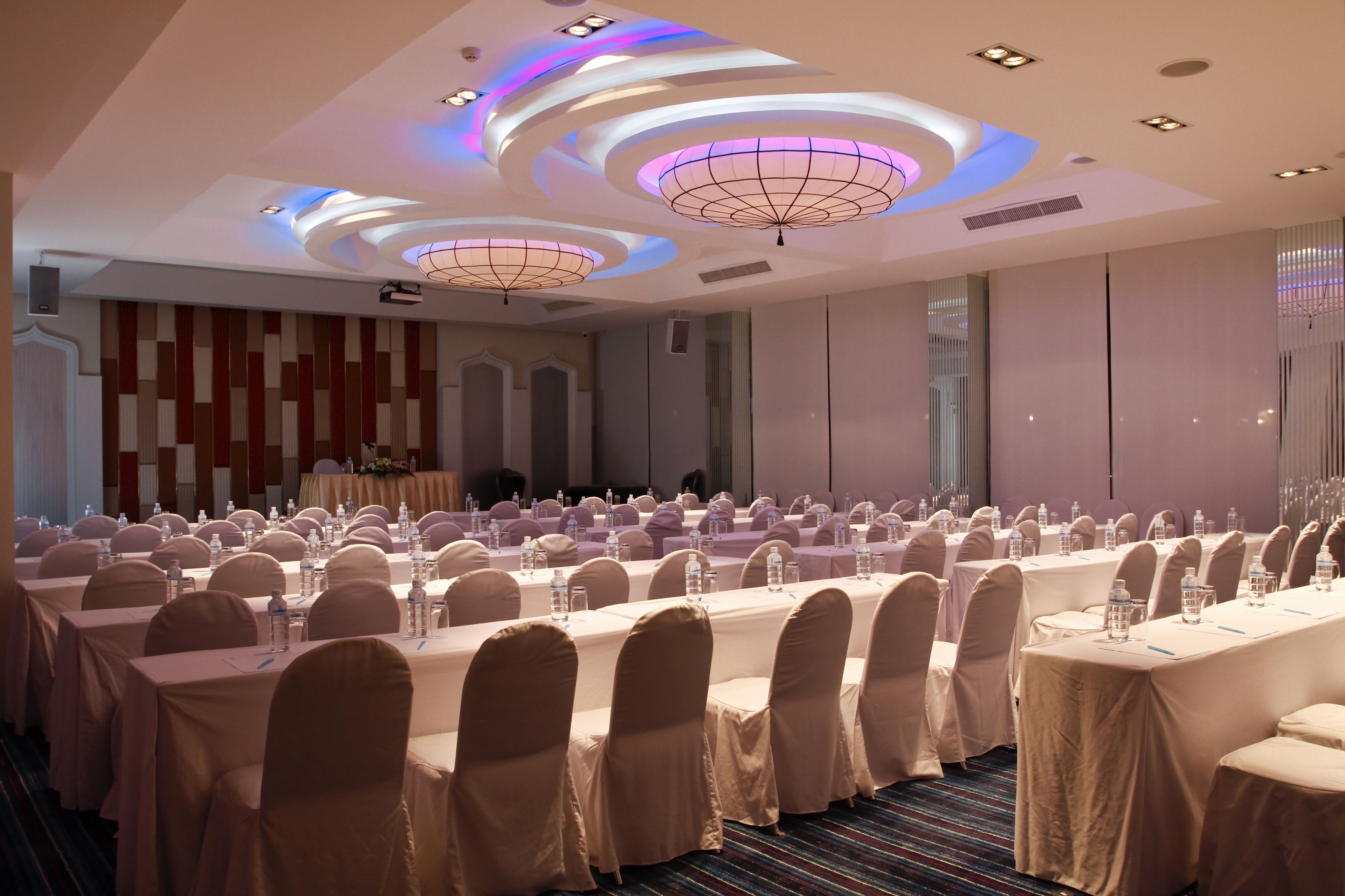 Un salón de conferencias con varias mesas, sillas y un escenario.