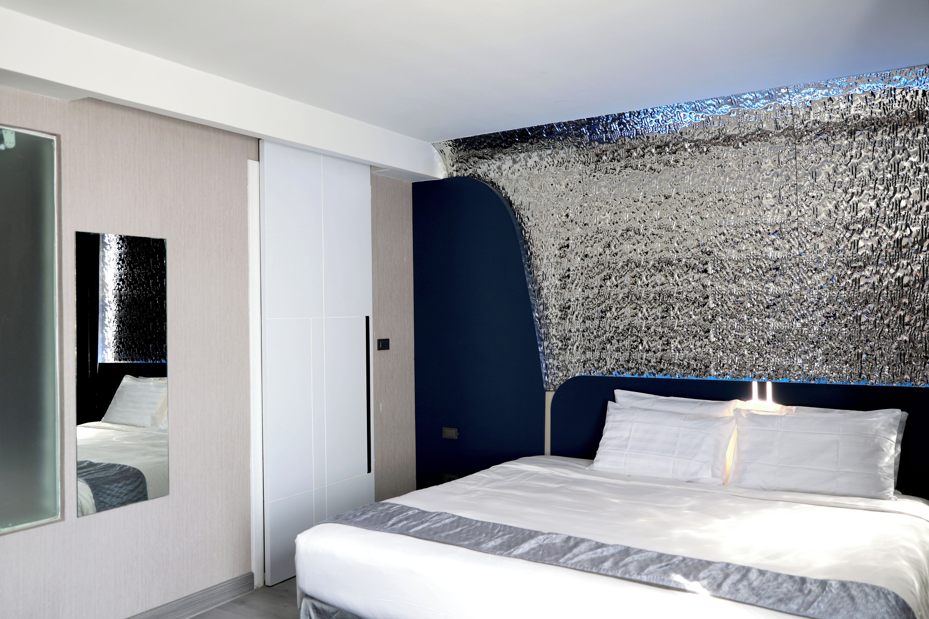 Un dormitorio moderno con cama, espejo y pared con textura.
