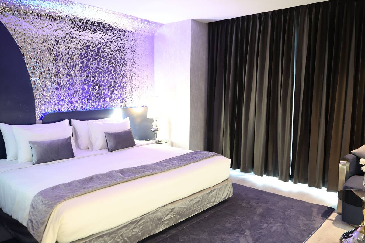 Una habitación de hotel moderna con una cama grande, una cortina oscura y un detalle decorativo en la pared.