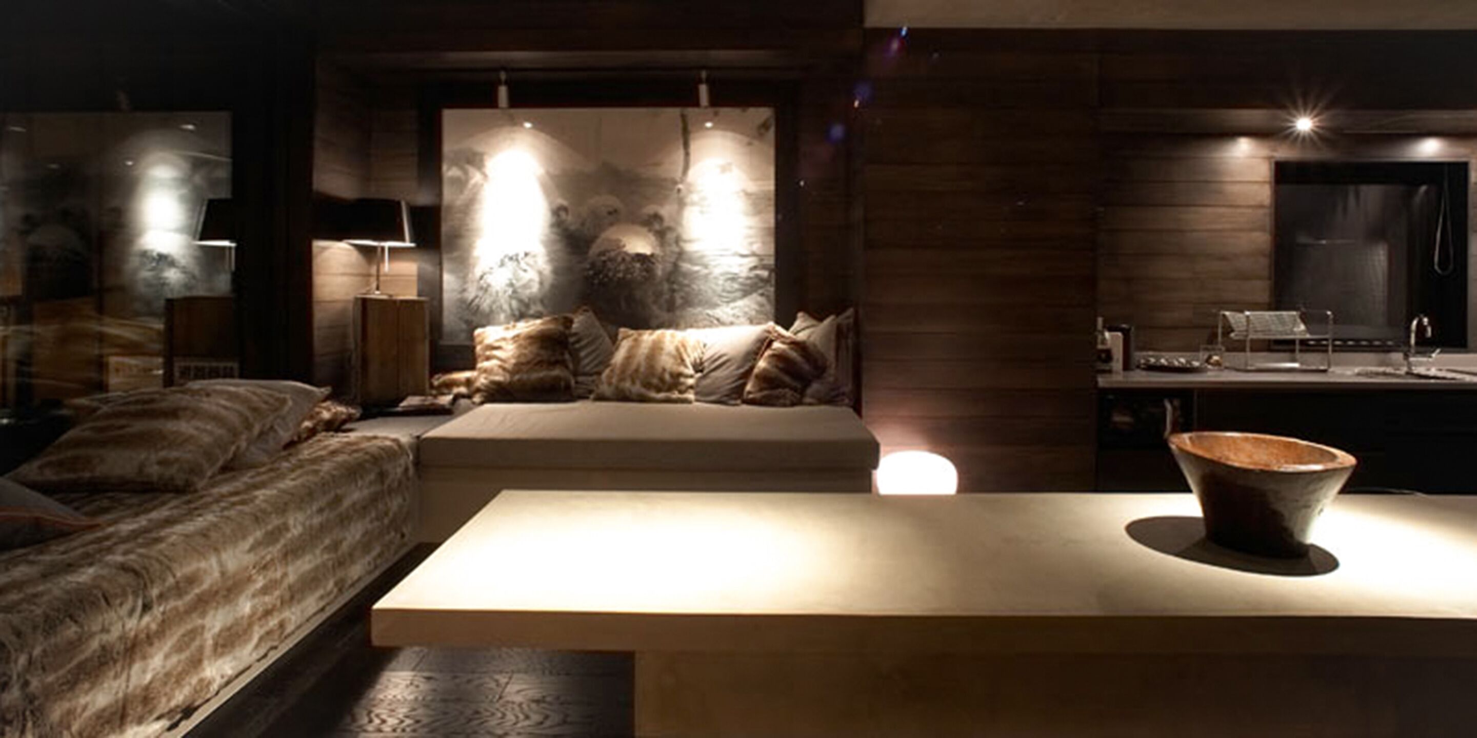 A modern bedroom with a large bed, a sofa, a dining area, and a large wall art piece.
