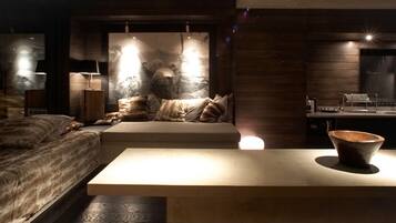 A modern bedroom with a large bed, a sofa, a dining area, and a large wall art piece.
