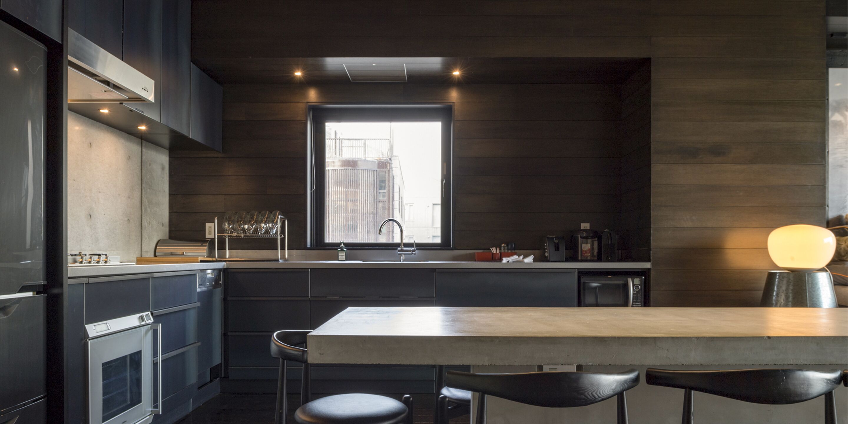 A modern kitchen with a central island, bar stools, and a window overlooking a cityscape.