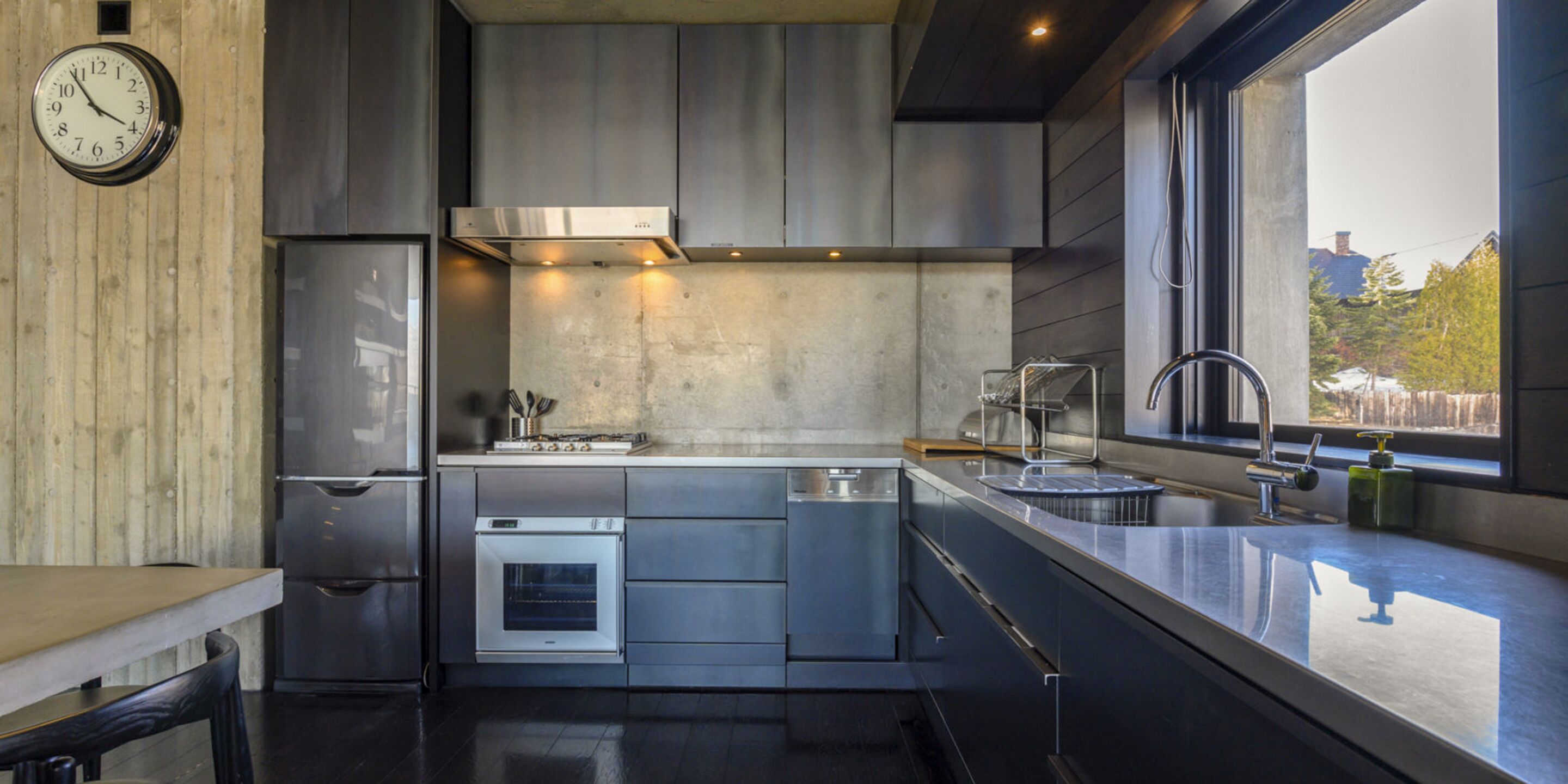 A modern kitchen with stainless steel appliances, a built-in oven, and a window providing a view of the outdoors.