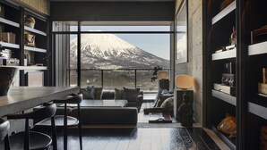 Ein modernes Interieur mit einem großen Fenster mit Blick auf einen verschneiten Berg, einer gemütlichen Sitzecke und einem Bücherregal voller Bücher und Dekoration.