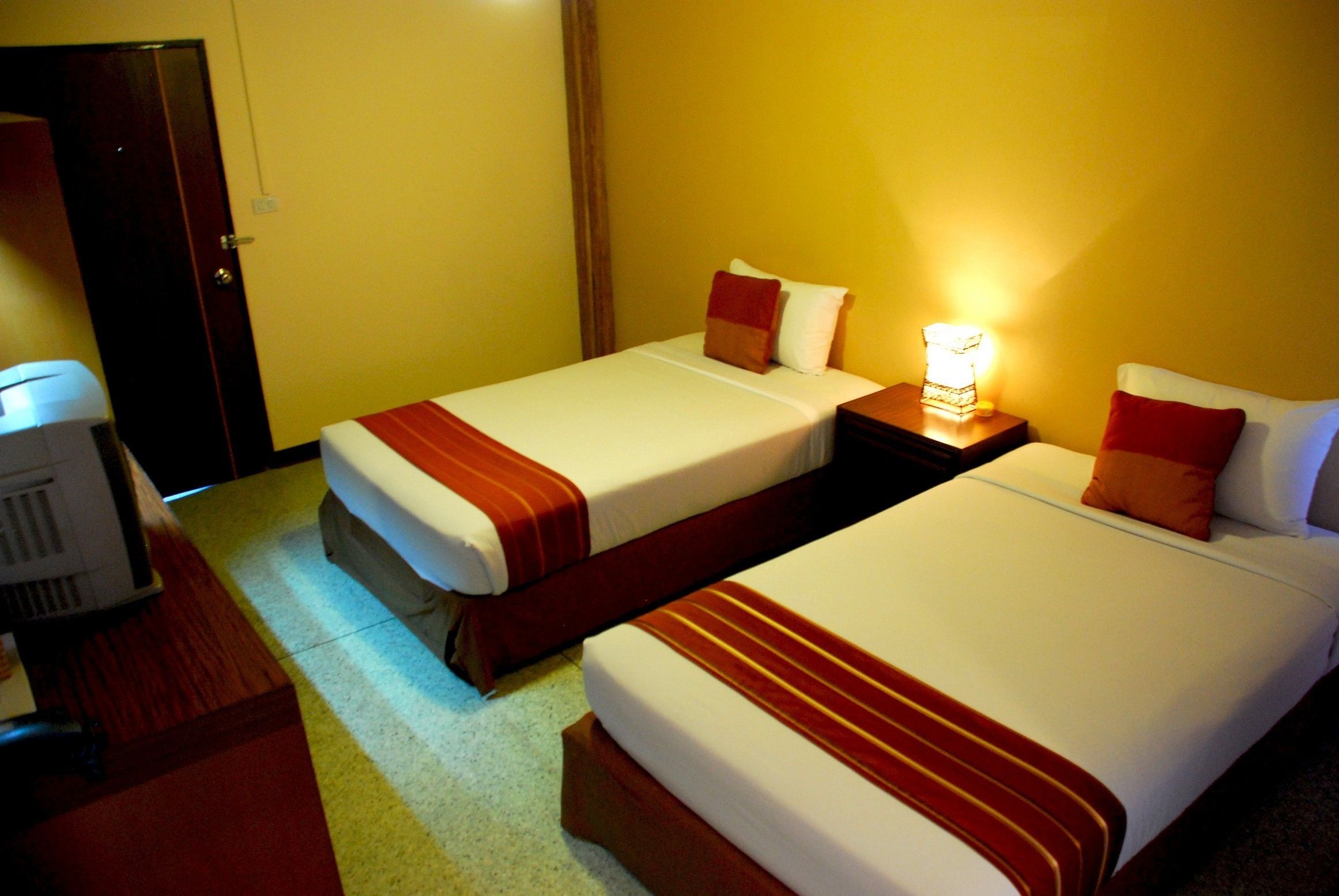 A hotel room with two beds, each with a red and white striped bedspread, a nightstand with a lamp, and a desk with a computer.